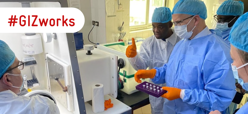 Five people in medical protective clothing and masks stand around a laboratory device.