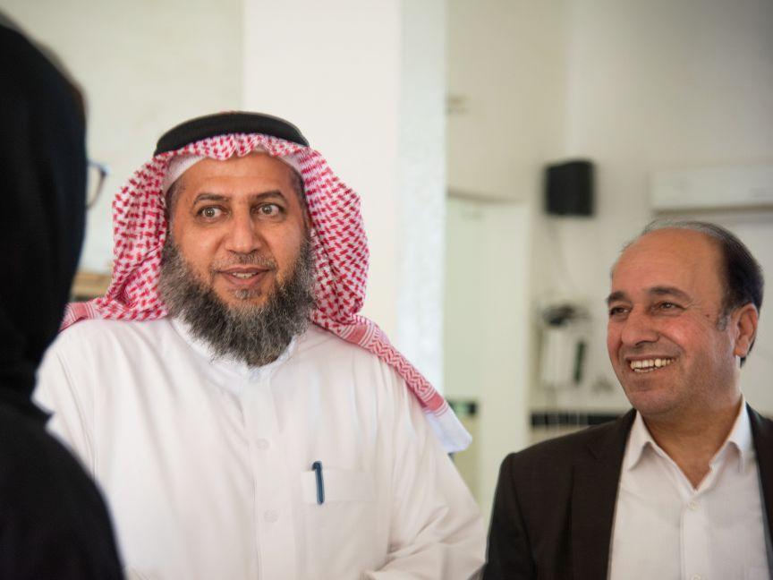 Zwei Männer, die einer Person außerhalb des Bilde freudig zuhören