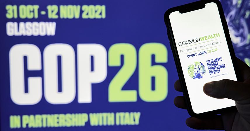 Auf der linken Seite ist ein Smartphone zu sehen mit dem Logo der COP26 in Glasgow. Im Hintergrund und leicht verschwommen ist der Schriftzug "COP26" zu erkennen sowie das Datum "31 OCT - 12 NOV 2021 und der Zusatz "in Partnership with Italy".