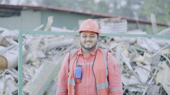 Ein Fabrikmitarbeiter steht in Schutzkleidung vor einem Zaun. (Photo: GIZ/Noor Alam)