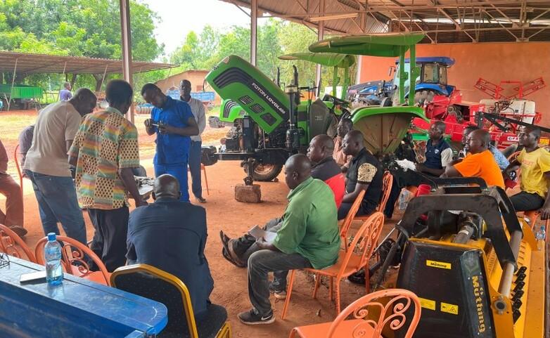 Menschen haben sich versammelt. Im Hintergrund befinden sich landwirtschaftliche Maschinen.