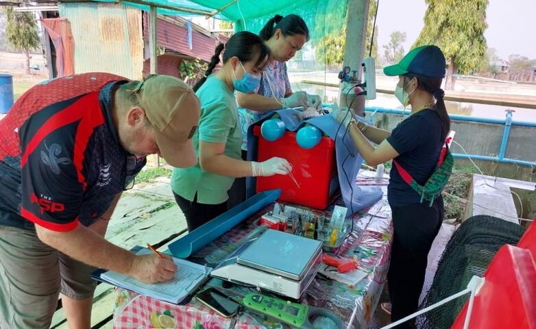 Drei laotische Frauen und ein Mann begutachten an einem Tisch im Freien den gefangenen Fisch.
