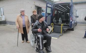 Ein Mann in einem Rollstuhl mit zwei Begleitpersonen neben einem Bus mit einer Rampe. Der Bus gehört zum „sozialen Taxidienst“ für Einwohner*innen, die aus gesundheitlichen Gründen oder wegen ihres Alters keine öffentlichen Verkehrsmittel nutzen können.