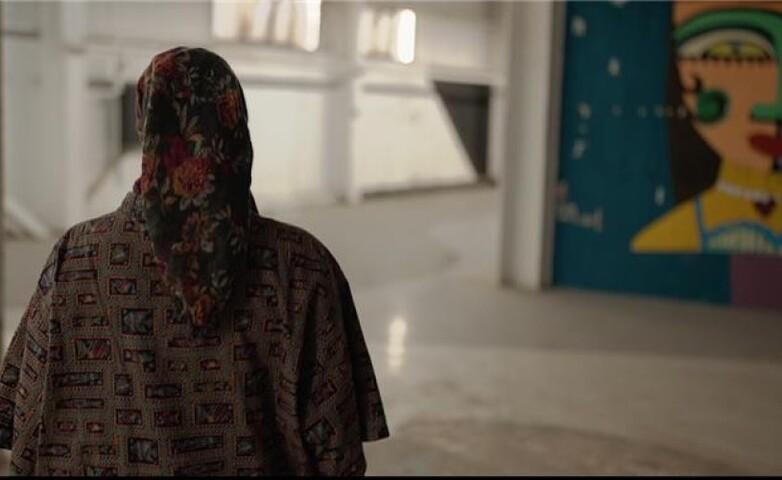 Eine Person steht in einer großen Halle. An der Wand im Hintergrund ist ein farbenfrohes Wandgemälde zu sehen.