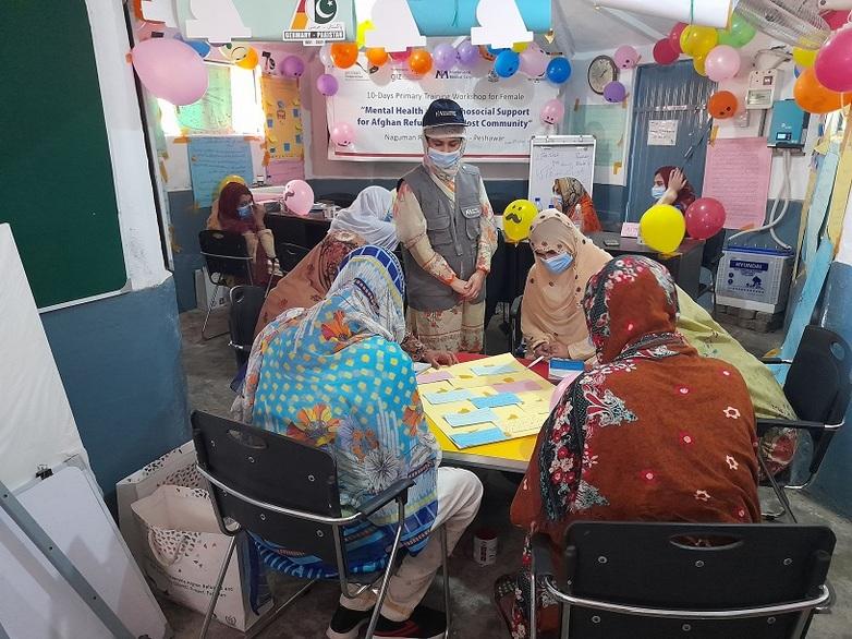 Junge Frauen sitzen an einem Tisch in einem mit Luftballons geschmückten Raum bei einem Workshop zu psychischer Gesundheit und psychosozialer Unterstützung. Copyright: GIZ