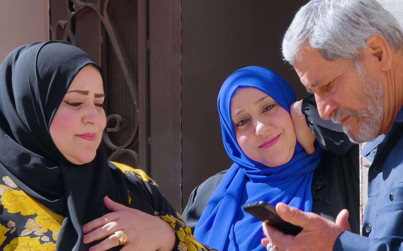 Zwei Frauen mit Kopftuch und ein Mann am Handy