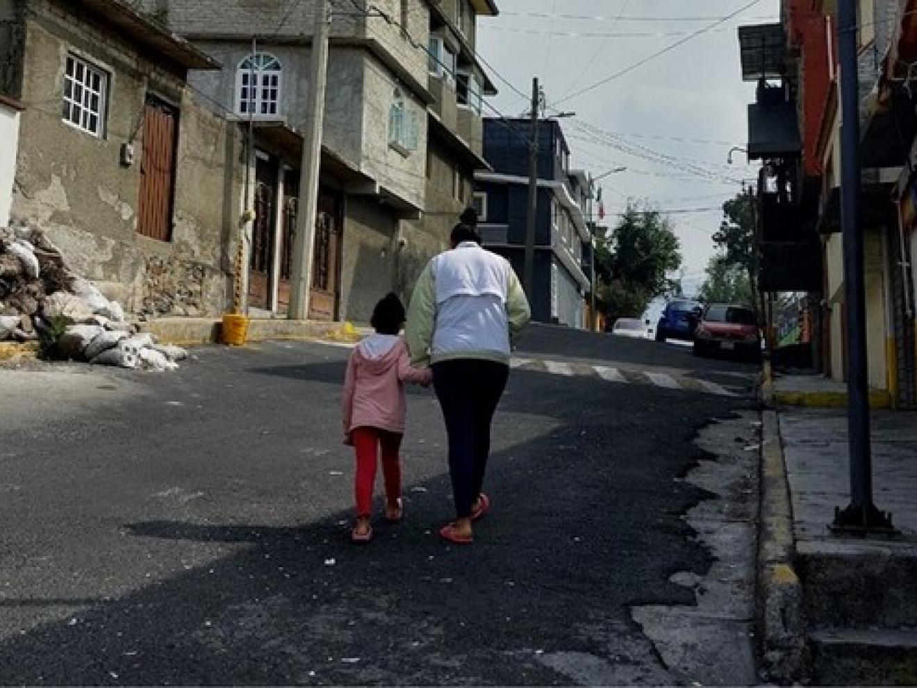 Frau läuft mit einem Mädchen an der Hand eine Straße hoch