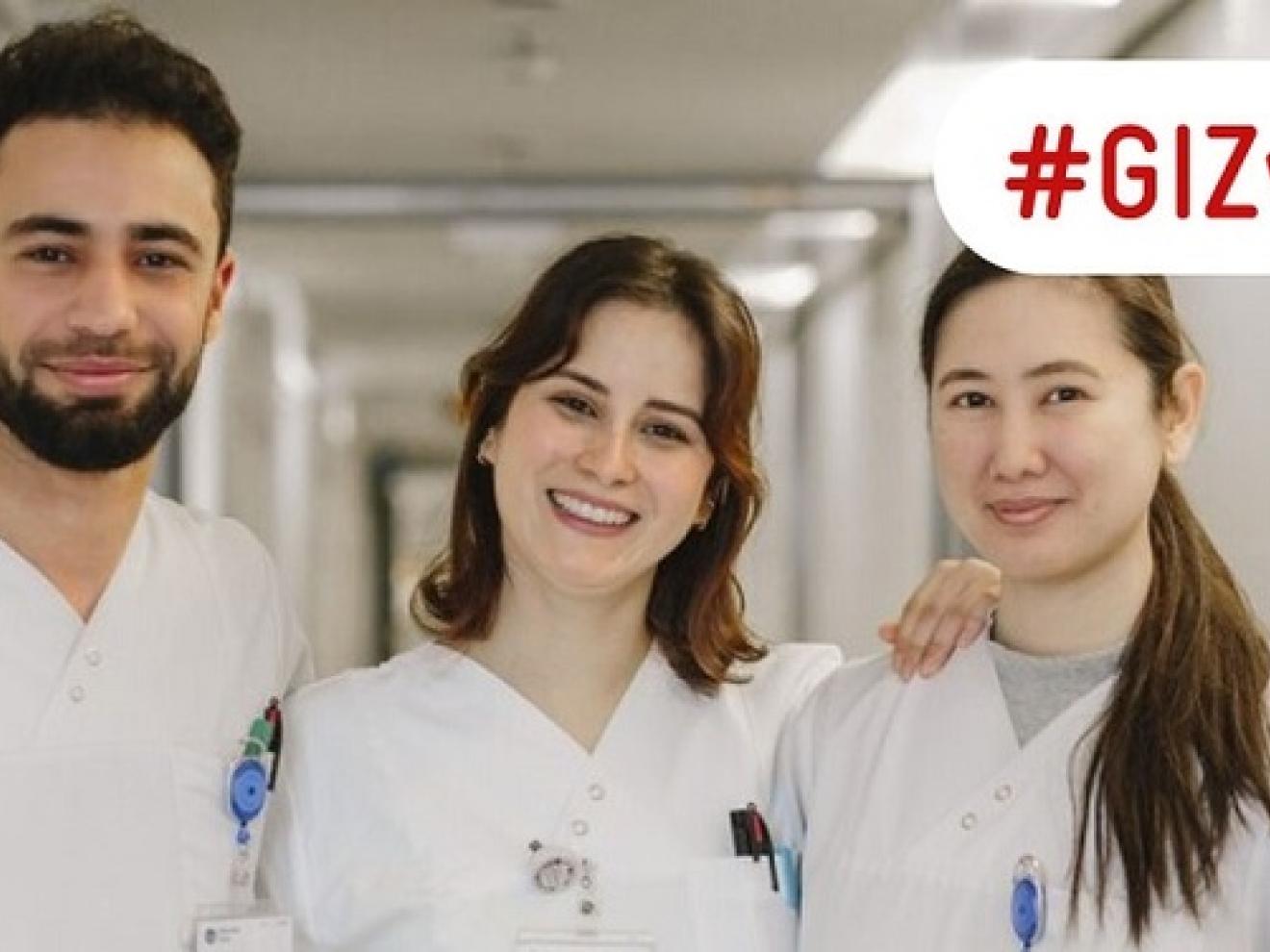 Drei Pflegefachkräfte stehen in einem Krankenhausflur und lächeln in die Kamera.