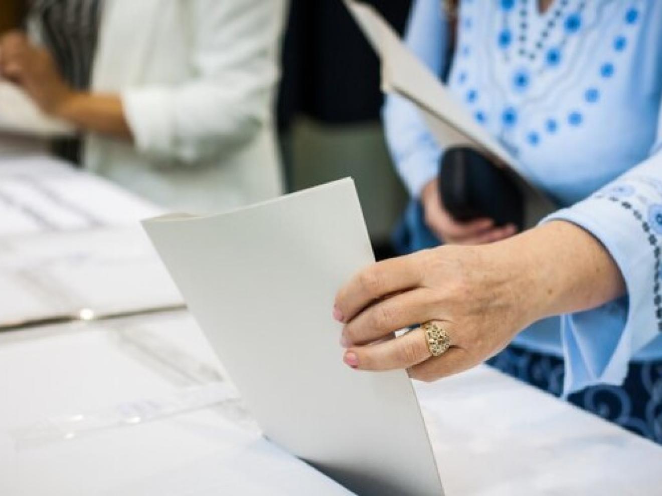 Eine Person gibt bei einer Wahl einen Stimmzettel ab.