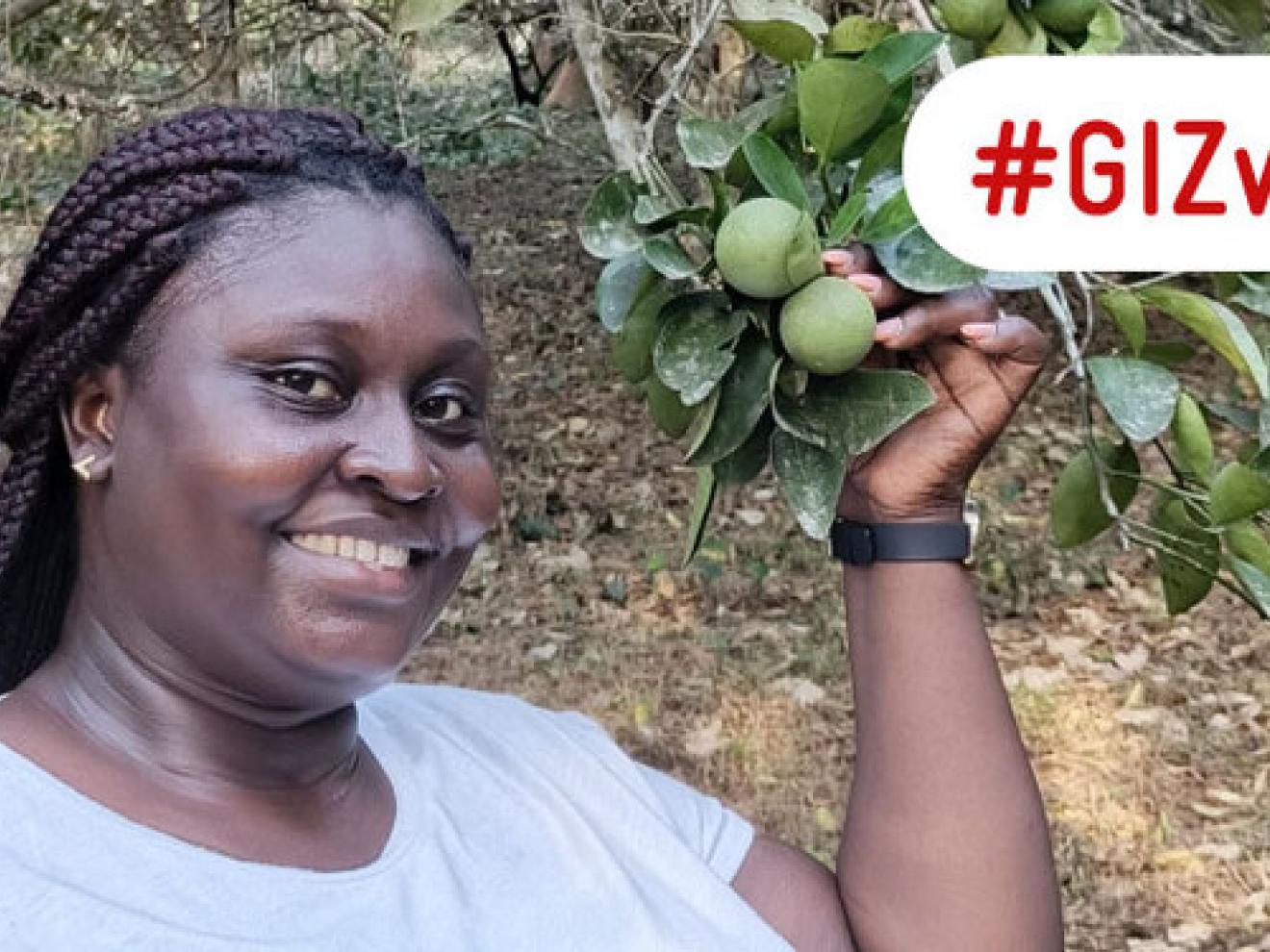A woman in a white T-shirt stands in front of a tree and smiles. In her left hand she holds a branch of limes. Next to it is the lettering “GIZ works”.