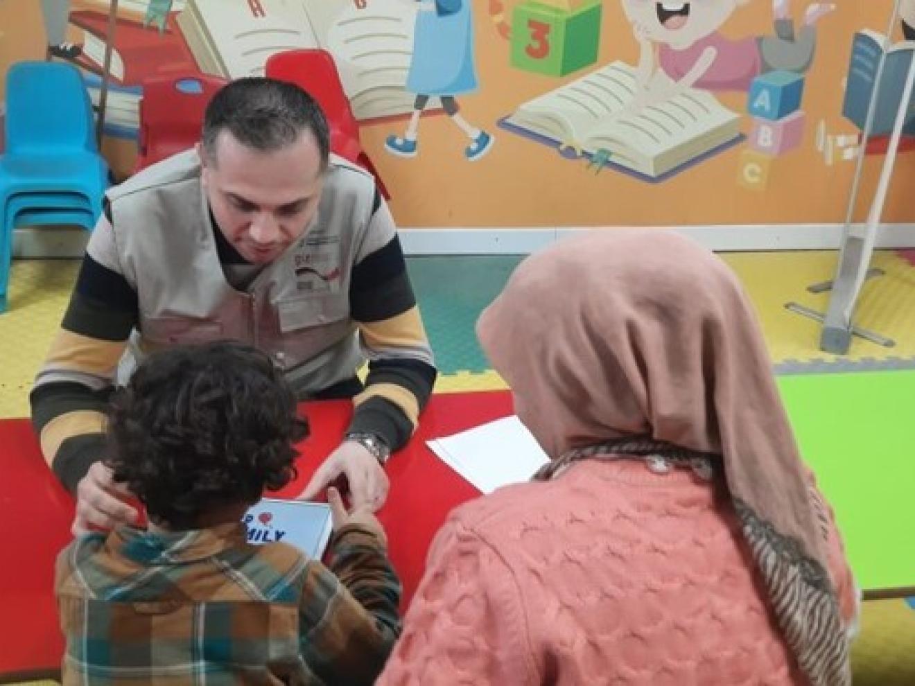Ein GIZ-Mitarbeiter sitzt mit einem Jungen und seiner Mutter in einem Kindergarten zusammen.