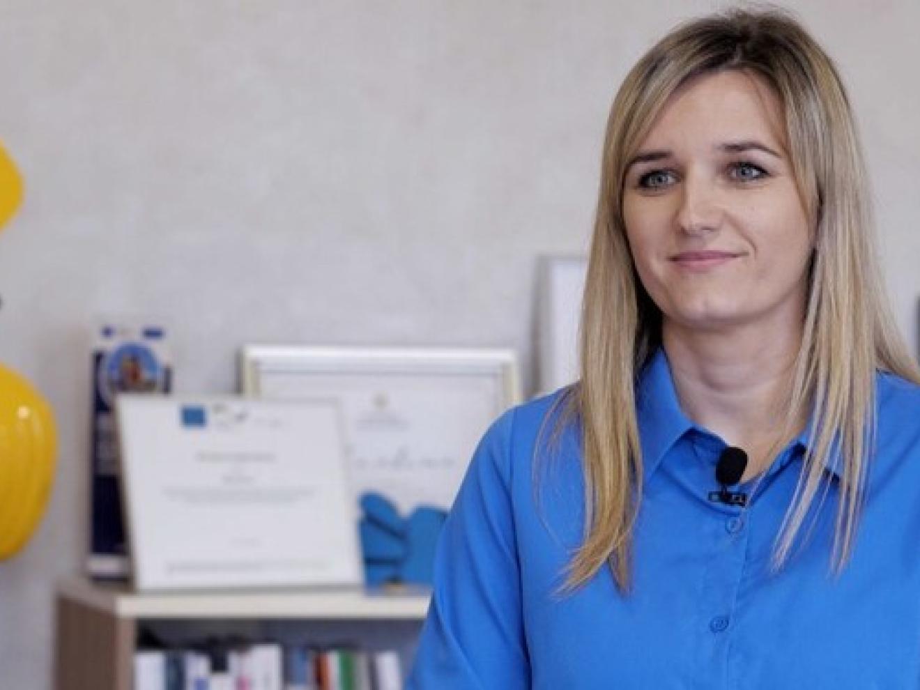 Naida Baručija sitzt vor einem Regal, auf dem eingerahmte Urkunden stehen.