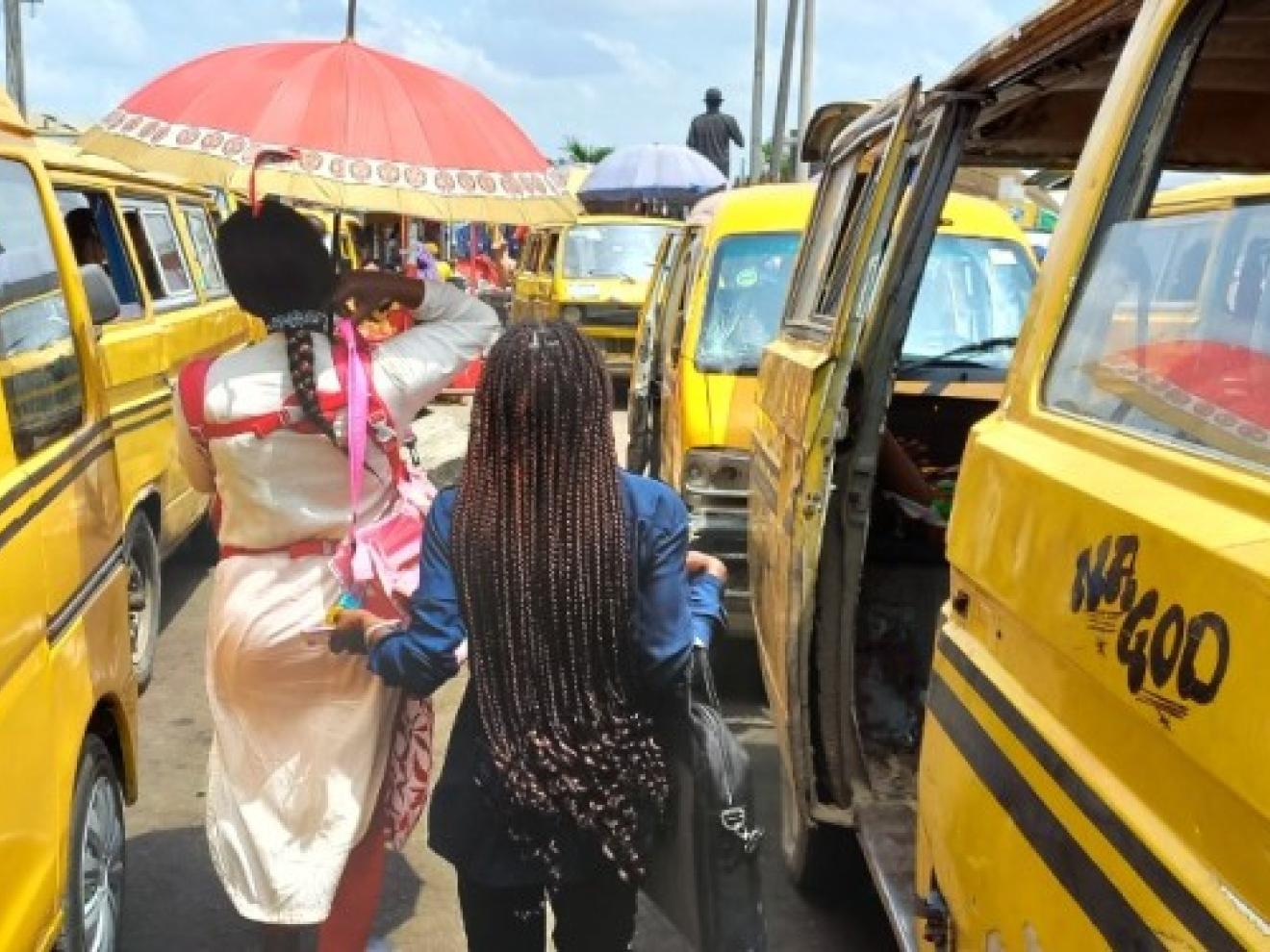 Zwei Frauen gehen zwischen gelben Taxibussen in der Großstadt Lagos (Nigeria) entlang.