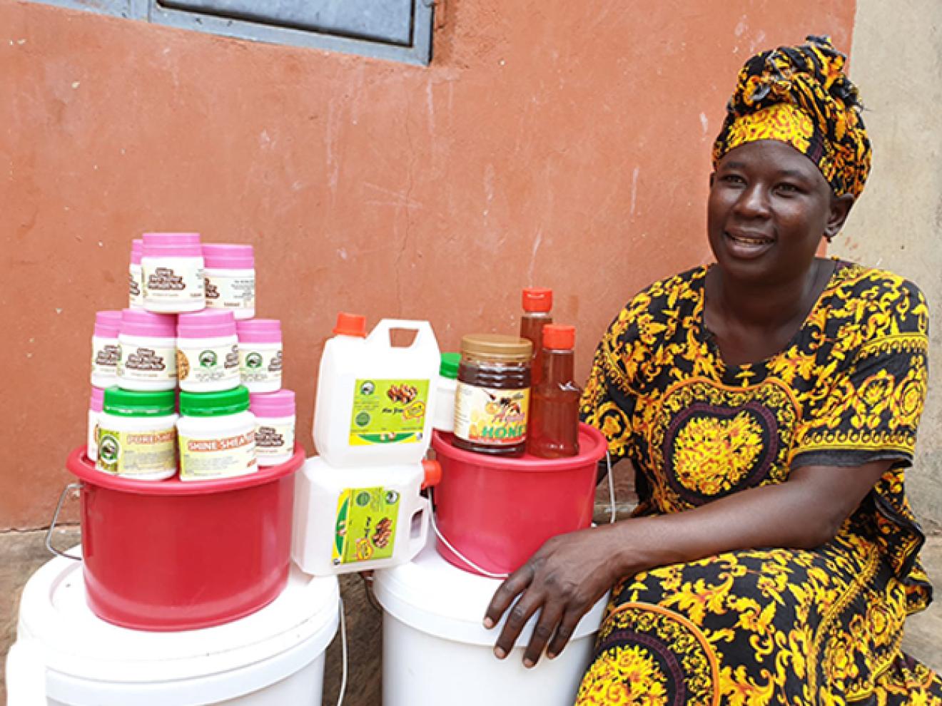 Eine Frau sitzt neben Behältnissen mit landwirtschaftlichen Erzeugnissen.