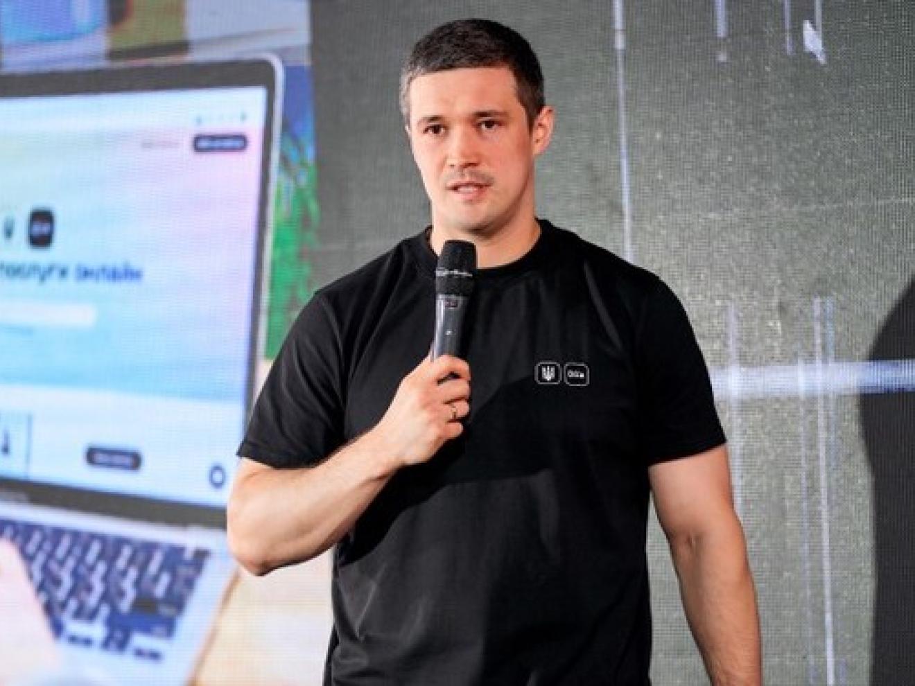 Ein Mann spricht in ein Mikrophon. Hinter ihm ist eine Präsentation zu Digitalisierung zu sehen.