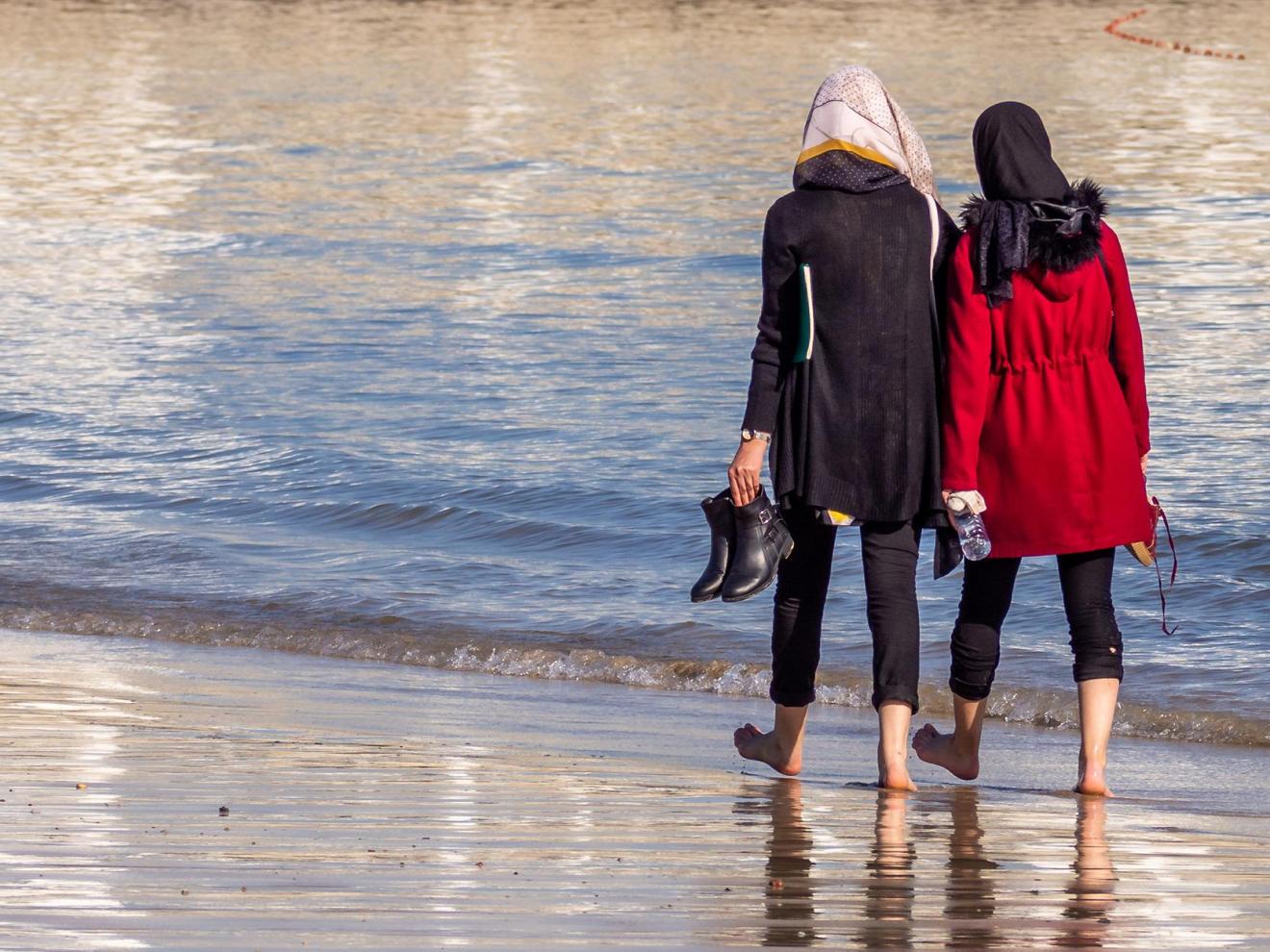 Zwei Frauen laufen am Strand mit dem Rücken zum Betrachter