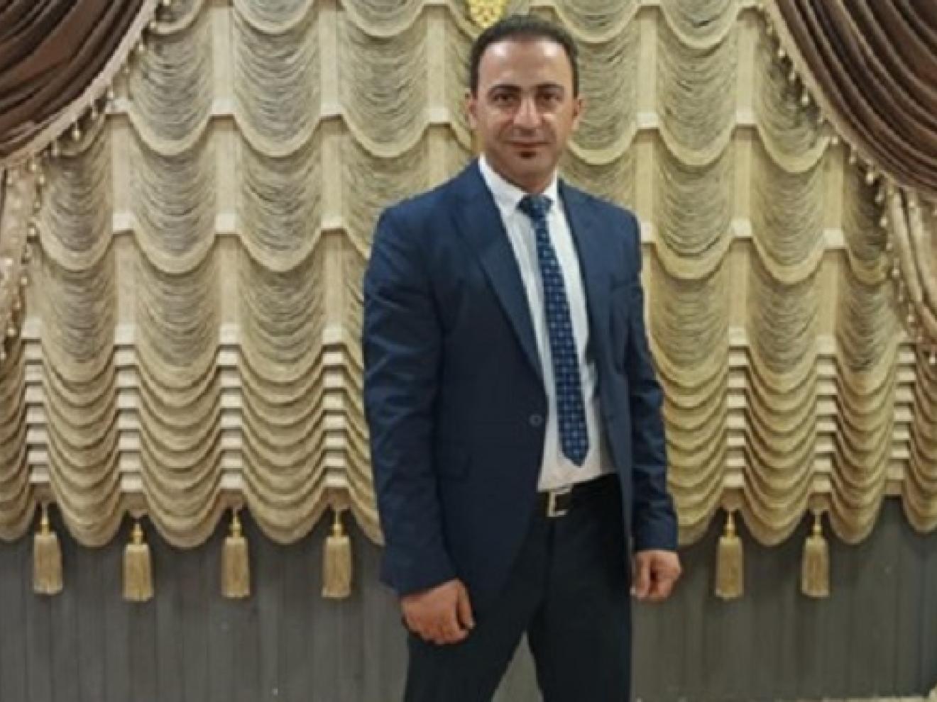 Ein Mann in einem Anzug mit Krawatte steht vor einer kunstvoll gerafften Vorhanginstallation in Gold-, Beige- und Brauntönen.