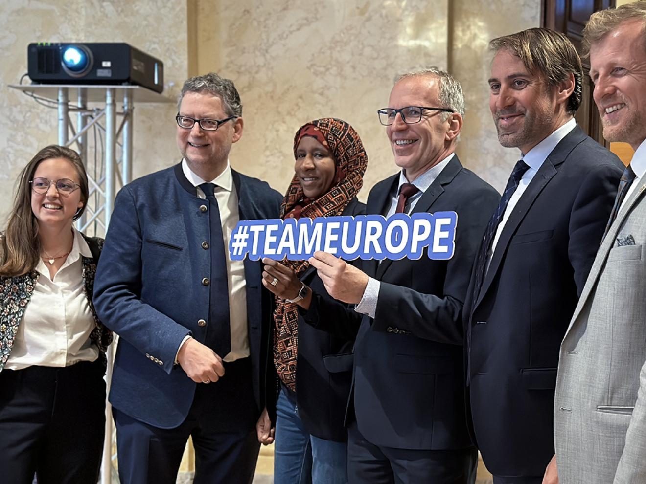 Sechs Personen posieren gemeinsam für ein Gruppenfoto, eine Person in der Mitte hält ein Schild mit der Aufschrift "#TEAMEUROPE".