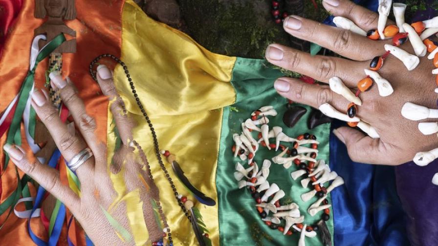Zwei Hände und indigener südamerikanischer Schmuck liegt auf einer Regenbogenfahne.